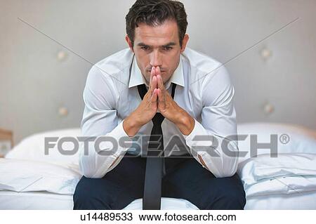 Stock Image - Overworked and stressed businessman sitting on the bed. Fotosearch