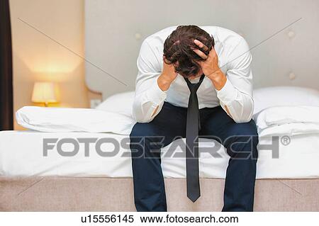 Stock Photography - Overworked and stressed businessman sitting on the bed. Fotosearch