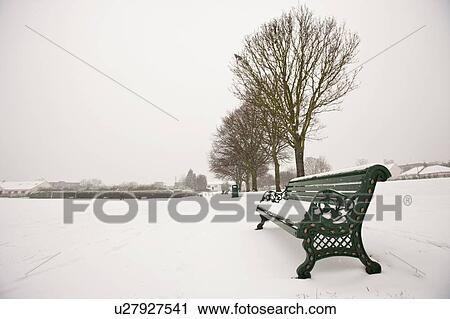 Stock Image - Park bench and park covered in snow. Fotosearch