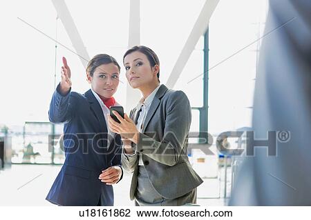 Stock Image - Passenger service agent assisting and giving directions with businesswoman in airport. Fotosearch