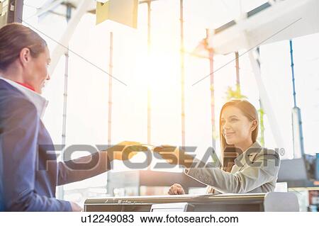 Stock Image - Passenger service agent giving boarding pass to young attractive businesswoman after check in at airport. Fotosearch