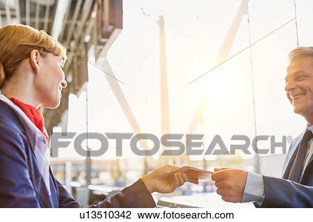 Stock Image - Passenger service agent giving boarding pass to mature attractive businessman after check in at airport. Fotosearch