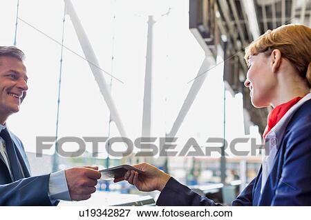 Stock Photo - Passenger service agent giving boarding pass to mature attractive businessman after check in at airport. Fotosearch
