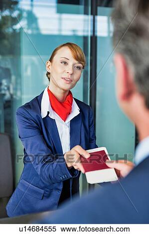 Stock Photography - Passenger service agent giving businessman passport and boarding pass in check in area at airport. Fotosearch
