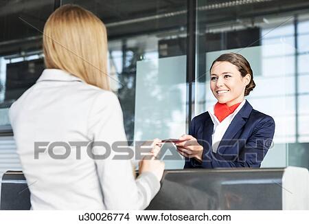 Picture - Passenger service agent giving woman's passport and boarding pass in check in area at airport. Fotosearch