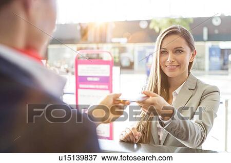 Stock Photo - Passenger service agent giving woman's passport and boarding pass in check in area at airport. Fotosearch