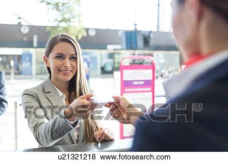 Stock Photo - Passenger service agent giving woman's passport and boarding pass in check in area at airport. Fotosearch