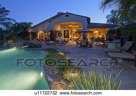 Stock Image - Patio with chaise lounge near swimming pool in manor house. Fotosearch