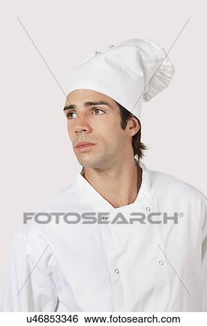 Stock Photograph - Pensive young man in chef's uniform looking away against gray background. Fotosearch