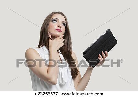 Pensive young woman holding tablet PC over gray background View Large Photo Image Stock Photo - Pensive young woman holding tablet PC over gray background. Fotosearch