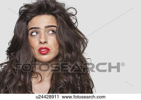 Stock Image - Pensive young woman with red lips looking sideways over gray background. Fotosearch