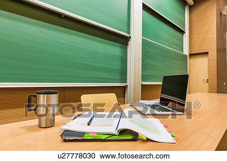 Stock Image - Photo of laptop on professor desk with tumbler and book. Fotosearch