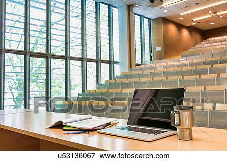 Stock Photo - Photo of laptop on professor desk with tumbler in classroom. Fotosearch