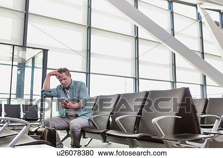 Photo of stressed mature man sitting while looking at his phone in airport View Large Photo Image Stock Image - Photo of stressed mature man sitting while looking at his phone in airport. Fotosearch