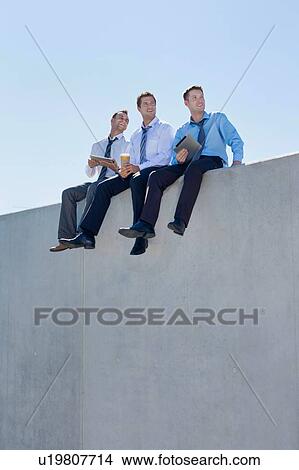 Photo of thoughtful businessmen sitting while using digital tablet in office rooftop View Large Photo Image Picture - Photo of thoughtful businessmen sitting while using digital tablet in office rooftop . Fotosearch