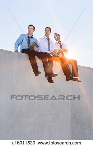 Stock Image - Photo of thoughtful businessmen sitting while using digital tablet in office rooftop . Fotosearch