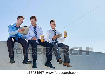 Stock Photo - Photo of thoughtful businessmen sitting while using digital tablet in office rooftop . Fotosearch