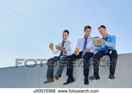 Stock Photo - Photo of thoughtful businessmen sitting and relaxing on rooftop . Fotosearch