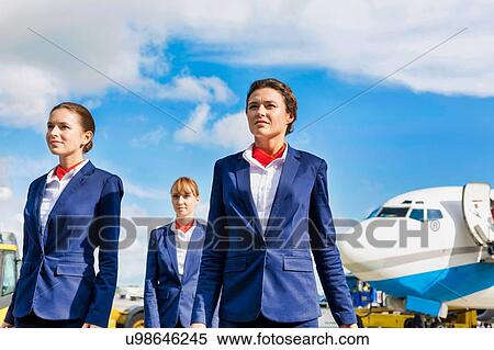 Stock Photography - Photo of three confident flight attendants walking against airplane in airport. Fotosearch