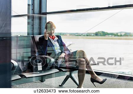Stock Image - Photo of young attractive airport staff sitting while talking on smartphone . Fotosearch