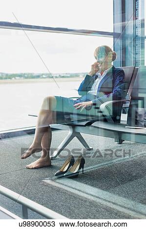 Stock Image - Photo of young attractive airport staff sitting while talking on smartphone . Fotosearch