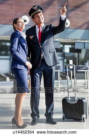 Picture - Pilot pointing aircraft while talking to flight attendant in airport . Fotosearch