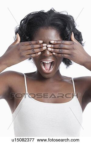 Stock Photo - Playful young woman covering eyes and shouting against white background. Fotosearch