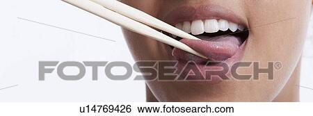 Stock Photograph - Playful young woman with chopsticks sticking out tongue against white background. Fotosearch