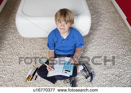 Portrait of a blond boy sitting near sofa doing homework View Large Photo Image Stock Photo - Portrait of a blond boy sitting near sofa doing homework. Fotosearch