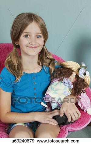 Stock Photo - Portrait of a Caucasian girl sitting on chair with doll. Fotosearch