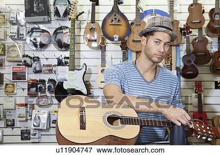 Portrait of a confident man restringing guitar in music store View Large Photo Image Stock Photo - Portrait of a confident man restringing guitar in music store. Fotosearch