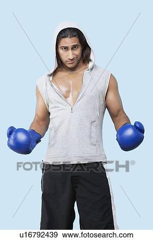 Portrait of a confident young man wearing boxing gloves standing over blue background View Large Photo Image Stock Photo - Portrait of a confident young man wearing boxing gloves standing over blue background. Fotosearch