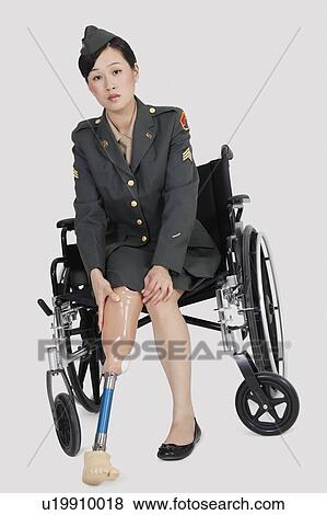 Stock Photo - Portrait of a female US military officer in wheelchair fitting prosthesis foot over gray backgrounds. Fotosearch