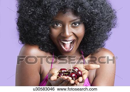 Stock Photograph - Portrait of a flirtatious young woman with fizzy hair holding cherries. Fotosearch