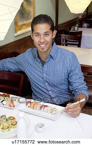 Stock Image - Portrait of a handsome young man eating sushi in Japanese restaurant. Fotosearch