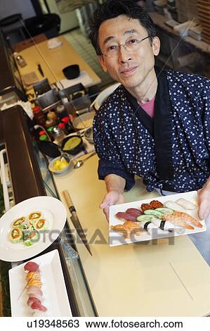 Stock Image - Portrait of a happy chef with Japanese sushi in restaurant. Fotosearch