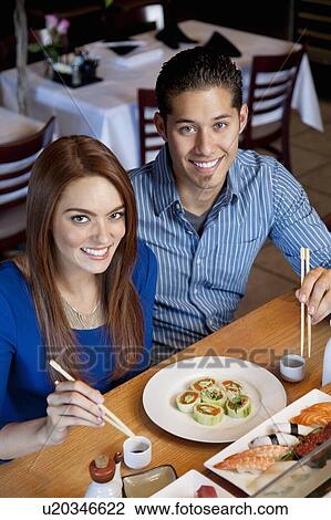 Stock Image - Portrait of a happy couple eating sushi with chopsticks in Japanese restaurant. Fotosearch