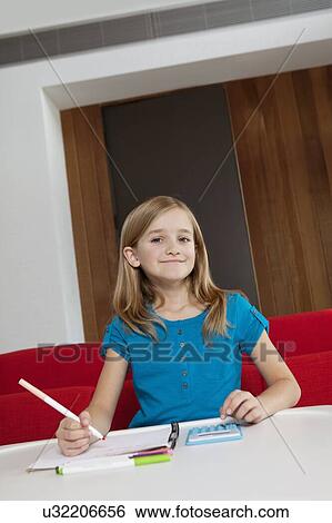 Stock Photograph - Portrait of a happy girl doing homework at table. Fotosearch