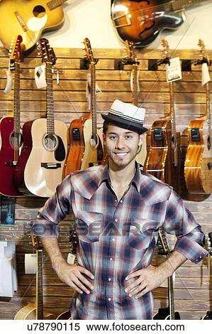 Stock Photography - Portrait of a happy music store owner standing in front of guitars. Fotosearch