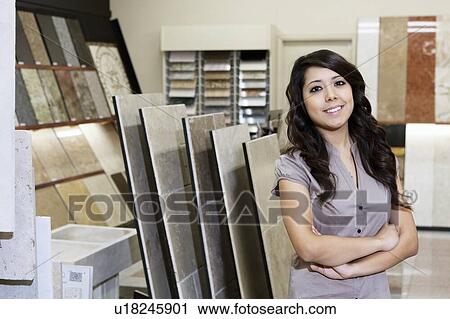 Stock Image - Portrait of a happy store clerk standing with arms crossed in tile shop. Fotosearch