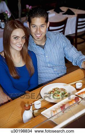 Picture - Portrait of a happy young couple in Japanese restaurant eating sushi. Fotosearch