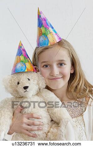 Portrait of a happy young girl wearing party hat with soft toy over colored background View Large Photo Image Stock Image - Portrait of a happy young girl wearing party hat with soft toy over colored background. Fotosearch