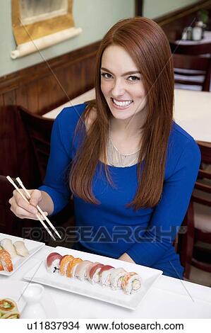 Picture - Portrait of a happy young woman eating sushi in Japanese restaurant. Fotosearch