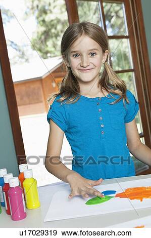 Stock Photo - Portrait of a little girl finger painting on paper at table. Fotosearch