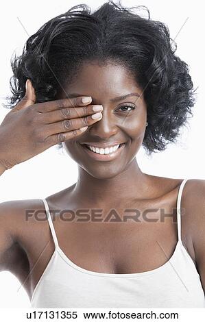 Stock Photography - Portrait of a playful young woman with hand over eye against white background. Fotosearch