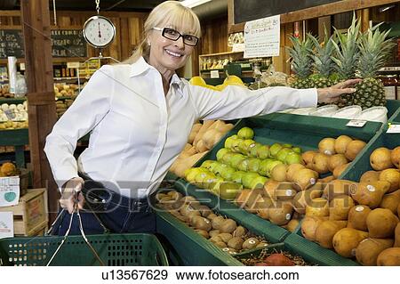 Stock Photo - Portrait of a senior woman shopping for pineapples in produce market. Fotosearch