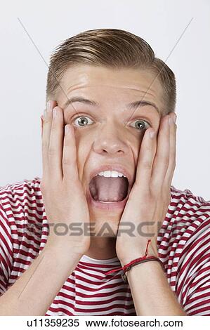 Portrait of a shocked young man with hands on face over white background View Large Photo Image Stock Photography - Portrait of a shocked young man with hands on face over white background. Fotosearch