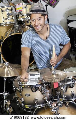 Stock Image - Portrait of a young customer with drum set in music store. Fotosearch