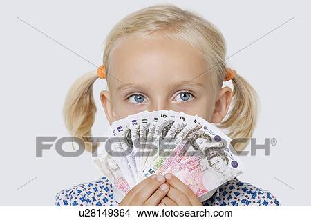 Picture - Portrait of a young girl covering mouth with fan of British currencies over white background. Fotosearch