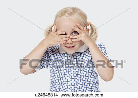 Picture - Portrait of a young girl peeking through fingers over white background. Fotosearch
